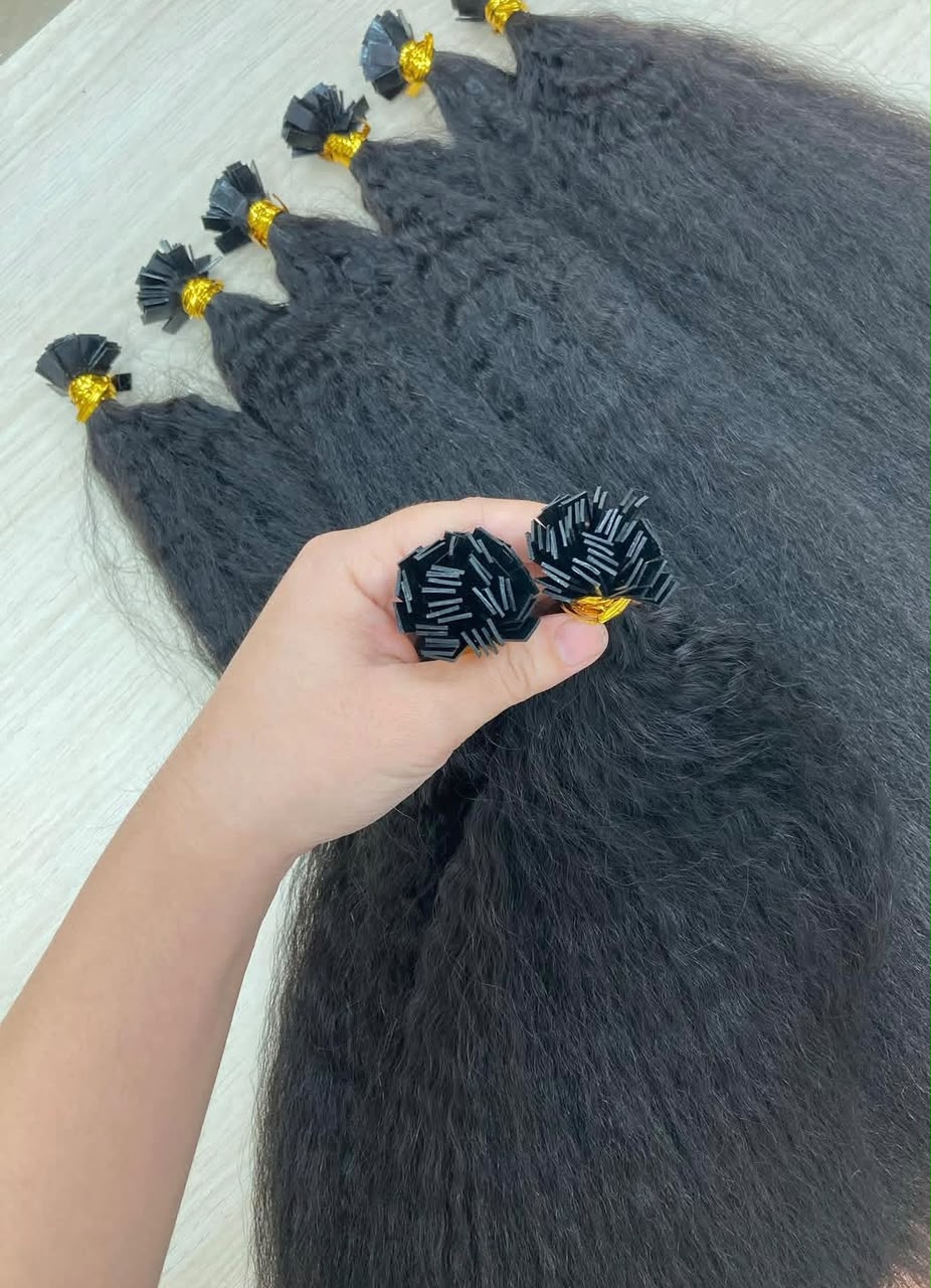 Raw kinky straight K-tip bundles in black with yellow bands, laid out with a hand holding a small bundle.
